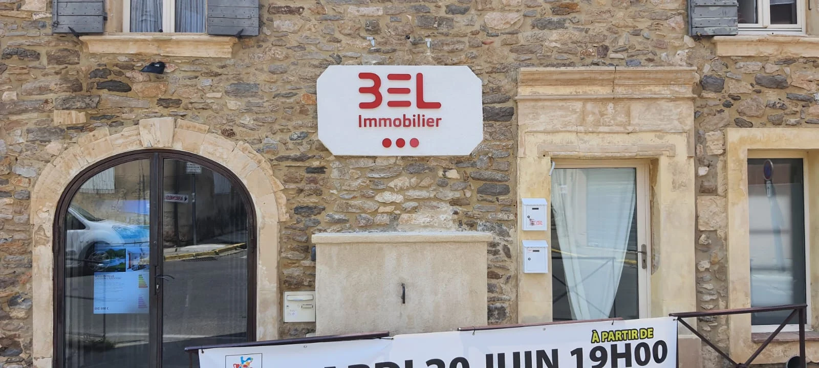 Vue large d’une façade en pierre avec panneau BEL Immobilier et portes vitrées