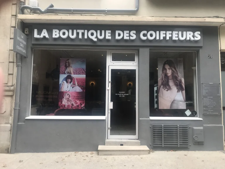 Devanture grise La Boutique des Coiffeurs avec lettres blanches et affiches en vitrine