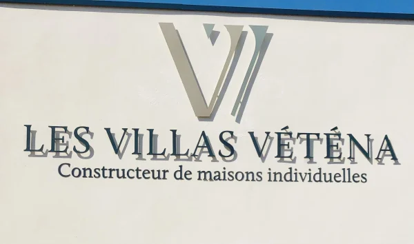 Logo et lettres grises Les Villas Véténa constructeur de maisons individuelles sur façade blanche