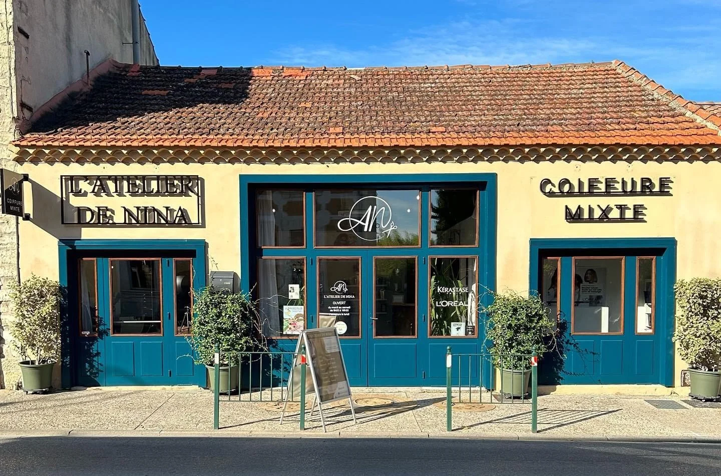Façade jaune et bleu canard de L’Atelier de Nina avec lettres noires Coiffure Mixte