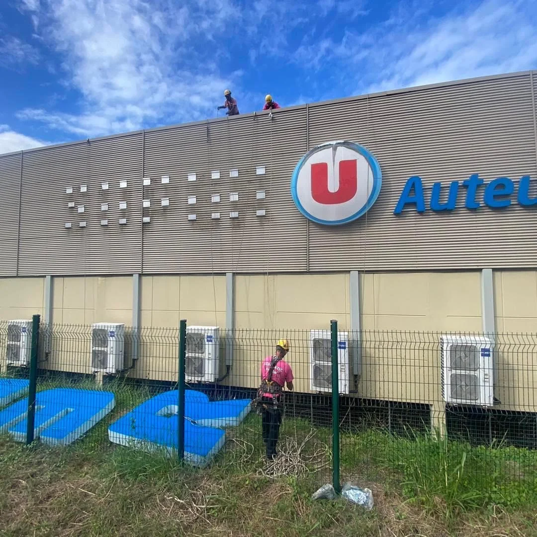 Techniciens installant une enseigne avec logo U et grandes lettres bleues sur une façade métallique
