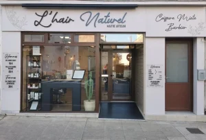 Façade blanche du salon L’hair Naturel avec enseigne coiffure mixte et barbier