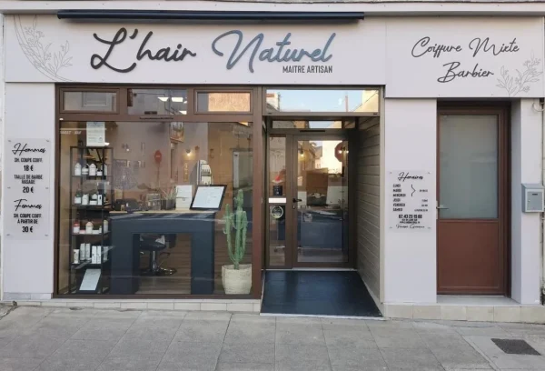 Façade blanche du salon L’hair Naturel avec enseigne coiffure mixte et barbier