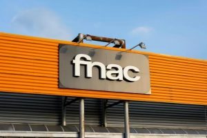 Logo Fnac en lettres blanches posé sur un panneau gris et une façade orange