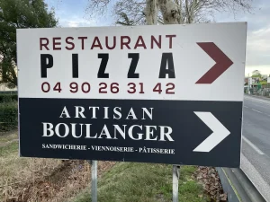Panneau en bord de route indiquant un restaurant-pizzeria et un artisan boulanger