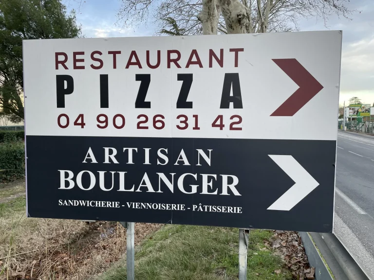 Panneau en bord de route indiquant un restaurant-pizzeria et un artisan boulanger