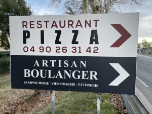 Panneau en bord de route indiquant un restaurant-pizzeria et un artisan boulanger