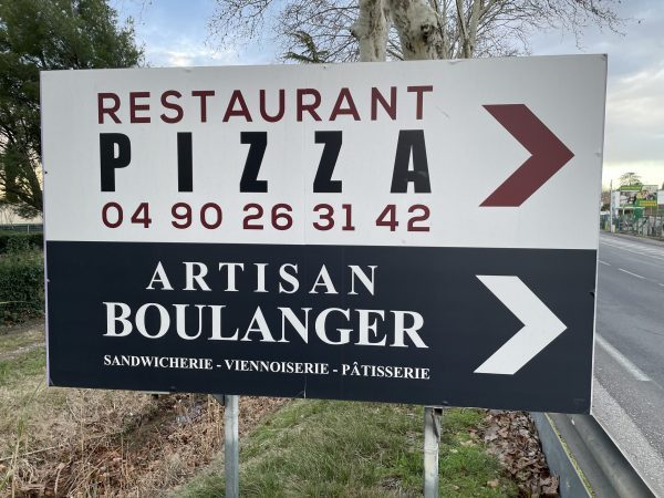 Panneau en bord de route indiquant un restaurant-pizzeria et un artisan boulanger