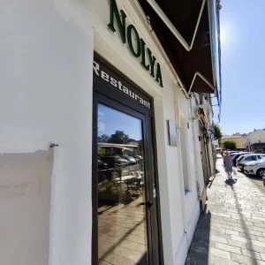 Entrée du restaurant Nolia sur un trottoir ensoleillé, avec enseigne visible