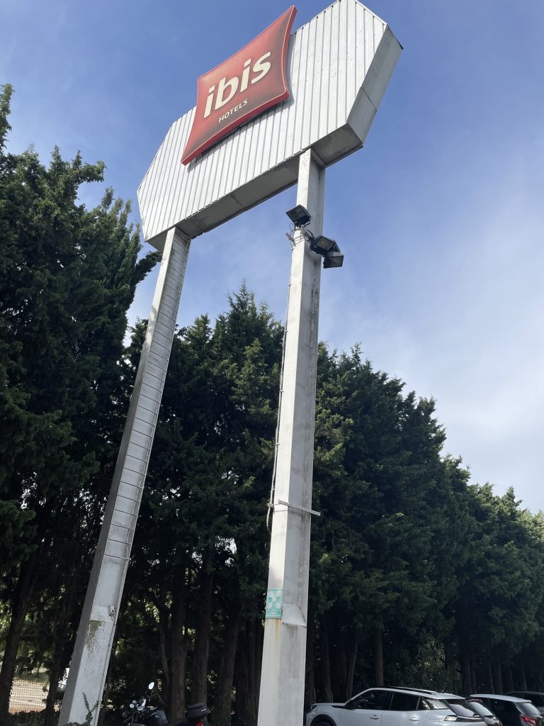 Contre-plongée détaillant le mât métallique et le panneau Ibis positionné en hauteur face au ciel
