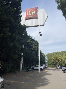 Totem Ibis en hauteur sur mât intérieur du parking, devant une rangée d’arbres