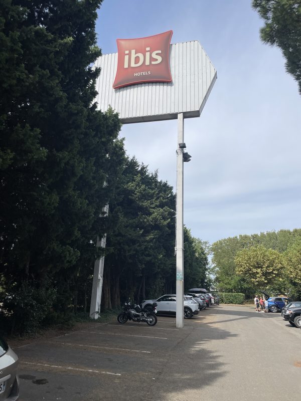 Totem Ibis en hauteur sur mât intérieur du parking, devant une rangée d’arbres