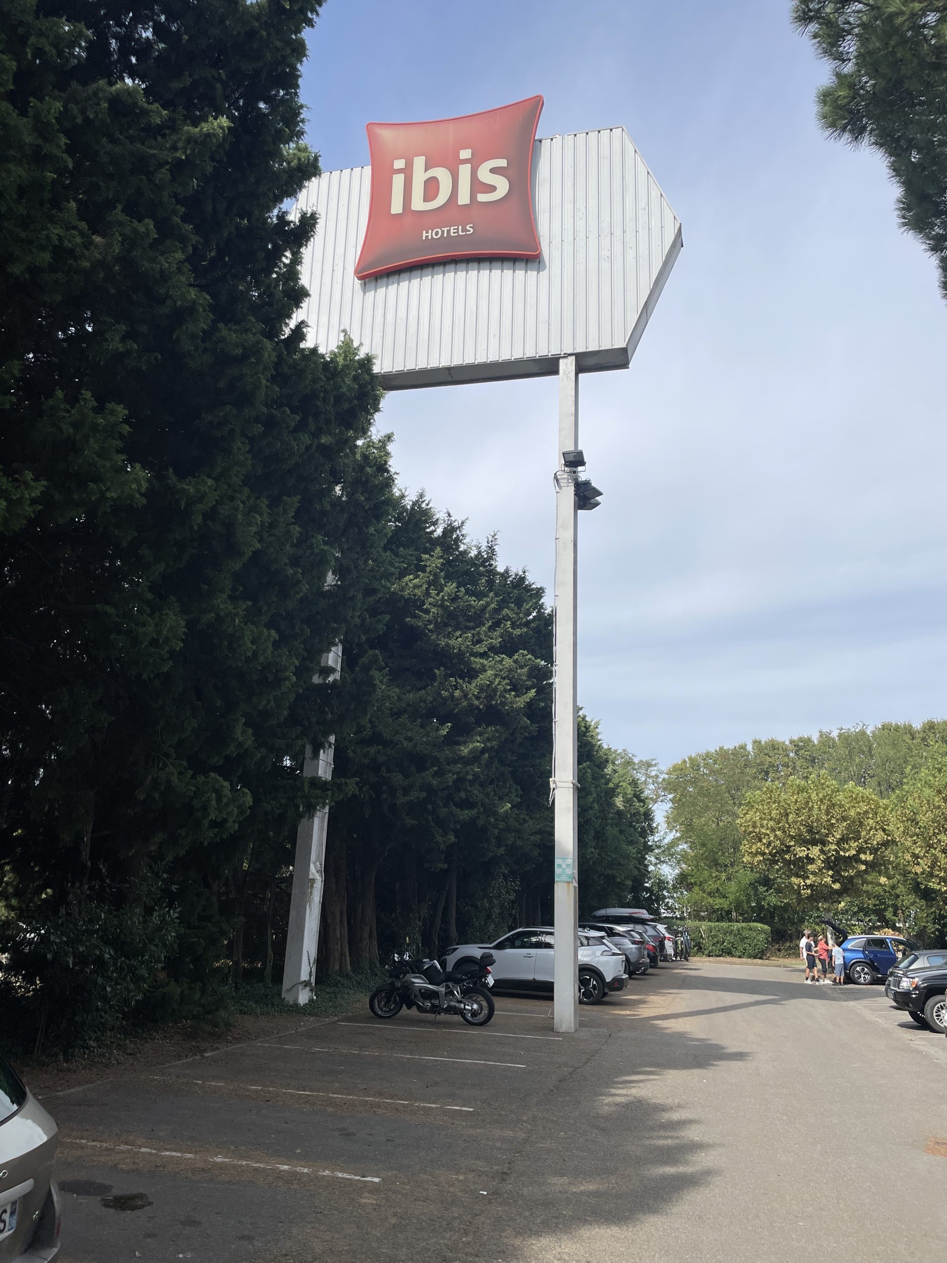 Totem Ibis sur mât visible depuis le parking Totem Ibis en hauteur sur mât intérieur du parking, devant une rangée d’arbres