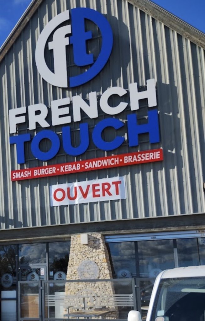 Détail vertical du grand lettrage 'French Touch' et du logo circulaire bleu et blanc sur façade métallique